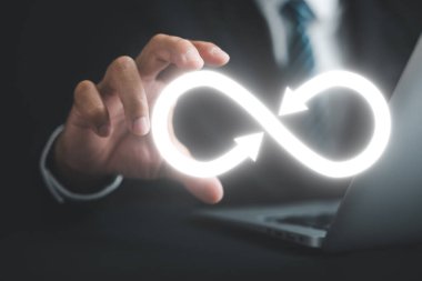 Karanlık arka planda işadamı tarafından tutulan dairesel sonsuzluk sembolü dairesel ekonomiyi ve sonsuz potansiyeli sembolize ediyor. Sürdürülebilir yatırım, bankacılık ve finansal büyüme stratejisi. sonsuzluk verisi