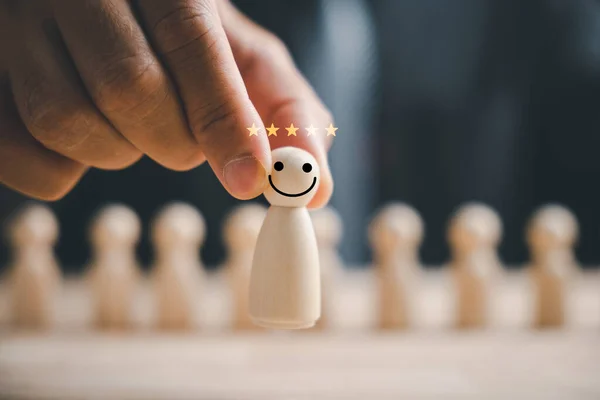 Hand-picking a wooden figure with a happy face for success. Customer service rating, feedback, and satisfaction survey. HR management choosing a positive team leader. HR or Human Resource Management