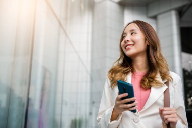 Happy business woman smiling using mobile phone outdoor walking on city street urban, Asian businesswoman texting smartphone commuting work she walking near her office building in morning