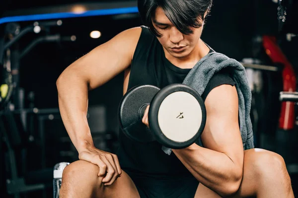 A handsome Asian man in sportswear holding a dumbbell, showcasing the benefits of exercise and training for physical and mental wellbeing. empty space