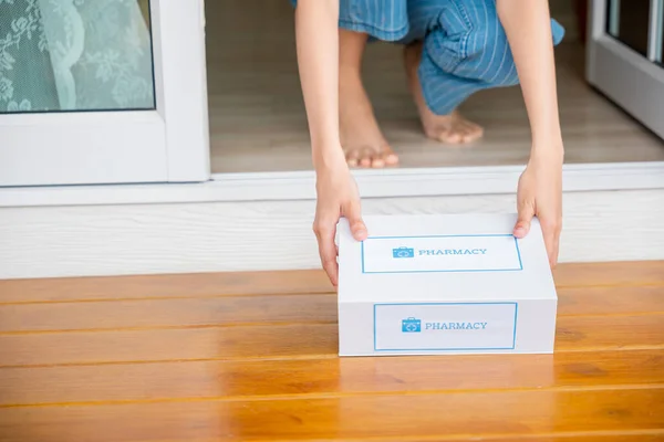 Close up hands of sick Asian woman sitting at door to receive medication first aid pharmacy box package from hospital delivery service at floor home, drugstore internet online medical business