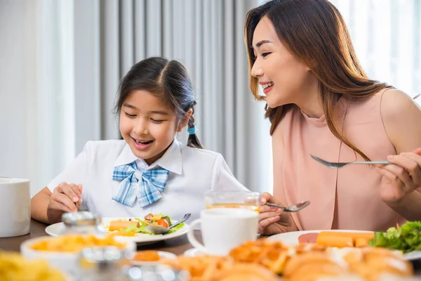 アジア系の朝食 笑顔の母親と子供の娘が食卓で朝食をとり 学校に行く前に家で健康的な食べ物 お母さんと小さな未就学児は一緒に楽しい食事をしています — ストック写真