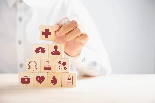 Wooden block held by hand displays healthcare and medical icons. Portrays safety, health, and family well-being, symbolizing pharmacy, heart care, and happiness. health care concept