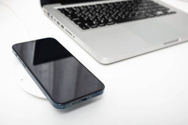 Bilgisayarın yanında kablosuz şarj cihazıyla akıllı telefon bataryası şarj ediliyor, modern teknoloji cep telefonunu merkez ofisteki çalışma alanı masaüstüne aktarıyor.