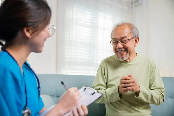 老人は自宅で医師に健康上の苦情について話す アジアの若い看護師は 家庭訪問中に話している間に処方クリップボードを書く高齢者 健康と医療の概念 — ストック写真