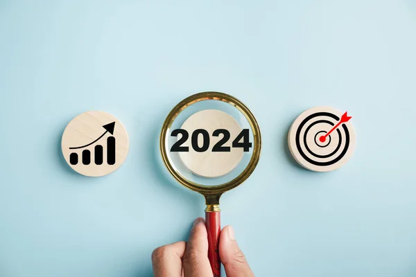 A magnifier highlights the 2024 icon, representing target business for year ahead. It signifies planning, project development, and investment ideas from the end of 2023 towards the new year concept.