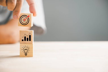 Bir iş adamı, stratejik bir iş planı ve eylem planını tasvir etmek için ustalıkla tahta blokları istifler. Bu kavram, mesleki alanda iş geliştirme ve büyümeyi temsil etmektedir..