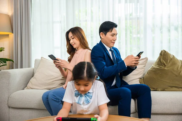 Family dont care about each other. Asian parents ignore their child and looking at their mobile phone at home, gadgets dependence overuse internet social media addiction on sofa living room