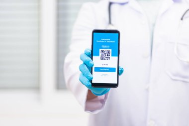 Tıbbi maskeli doktor, uygulamalı akıllı telefon dijital aşılı pasaport Coronavirus COVID-19 sertifikası gösteriyor.