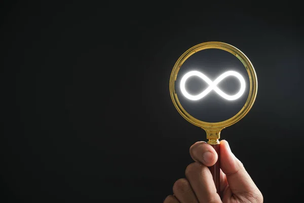 Magnifying glass focuses on infinity symbol icons, representing future sustainable investment growth. Technology and data concept. essence of future-focused investment. Technology infinity data