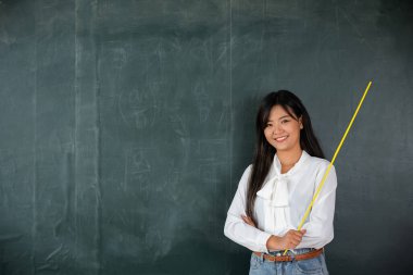 Okul konseptine geri dönelim. Asyalı bayan öğretmen, okulda tahtaya tahta sopayla gülümsüyor, kameraya bakan mutlu, güzel bir kadın, eğitime bakıyor.