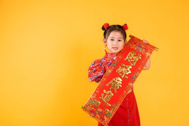Çin Yeni Yılı. Kırmızı Cheongsam Qipao Bahar Festivali çifti giyen mutlu Asyalı küçük kız çocuğu gülümsemesi Karakter FU servet, bereket ve sarı arka planda kısa süreli stüdyo demek.