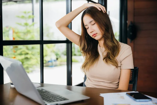 Tired office woman sitting at desk touching massaging stiff neck while holding her head in cafe, Asian business woman suffering from neck ache pain caused by sitting working long time laptop usage