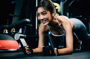 Formda genç bir kadın, iç spor salonunda egzersiz yaparken denge ve dayanıklılığını arttırmak için denge topunun üzerinde kalas pozisyonunu koruyor, koyu renk spor arka planında egzersiz yapıyor.