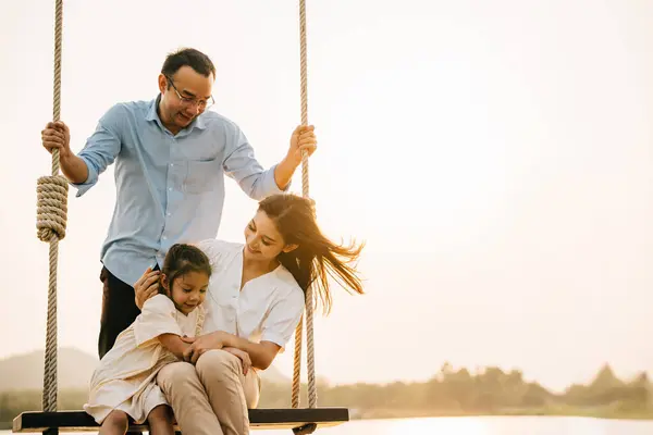 Asian family swinging on a swing in a serene nature setting, feeling the happiness and the joy of being active and playful in the outdoors, Happy Family Day