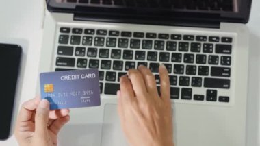 Bilgisayardaki kredi kartlarıyla kadın kaydının en üst görüntüsü elektronik ödeme güvenliğini çevrimiçi yapıyor, kadının elleri kredi kartı tutuyor ve evde ürün alımıyla birlikte dizüstü bilgisayar kullanıyor, İnternet üzerinden alışveriş yapıyor.