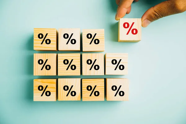Concept of interest rate and financial ranking. Businessmans hand placing a wooden cube block with a percentage symbol icon, highlighting the importance of monitoring rates.