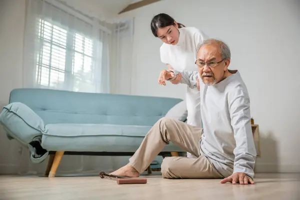 Dizziness elderly old man falling down lying on floor with walking stick and assistant nurse help to support, senior father fall on the ground and his daughter helping wake up and get up, accident