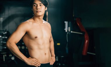 Kas yapısı ve parlak gülüşü olan genç bir adam, spor salonunun içinde duruyor, atletik fiziğini ve kaslarını gösteriyor, formda oluşuyla gurur duyuyor. Kopya alanı ile Sağlıklı Yaşam Biçimi