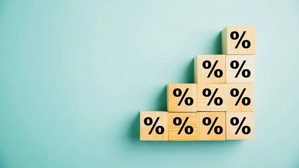 Concept of interest rate and mortgage rates. Hand putting a wooden cube block on top, representing growth and an upward direction, with an accompanying percentage symbol.