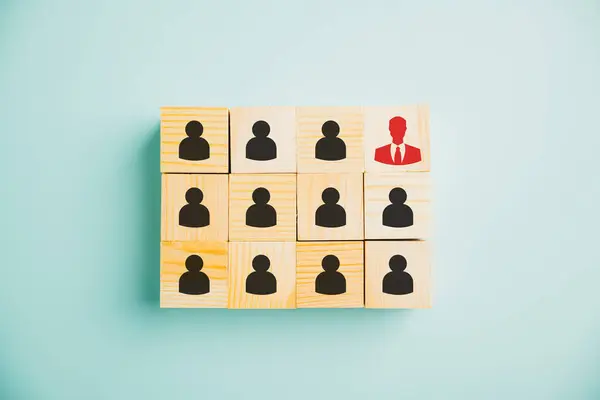 On a wooden block, a red manager icon catches staff employee icons, symbolizing significance of leadership and differentiation in business world. Depicts concept of human development and individuality