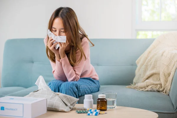 Sick woman. Asian young girl cold sick she sneeze with tissue paper on sofa, beautiful female health problem blowing nose use pharmacy kit box delivery service from hospital, delivery pharmacy concept