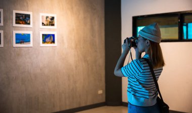 Asyalı kadın, çerçeveli resimlerin önünde resim galerisi koleksiyonu çekiyor beyaz duvarda kameralı resimler, fotoğraf çerçevesinde fotoğrafçı saati sergi sanat galerisine yaslanıyor.