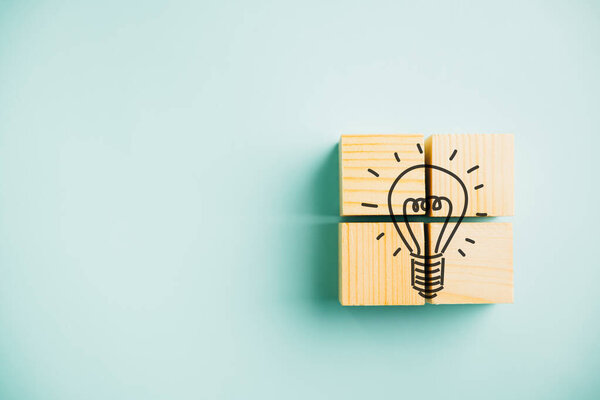 Creative concept represented by wooden cube with light bulb icon on blue background. Teamwork and brainstorming session for generating new business ideas and selecting the best solutions.