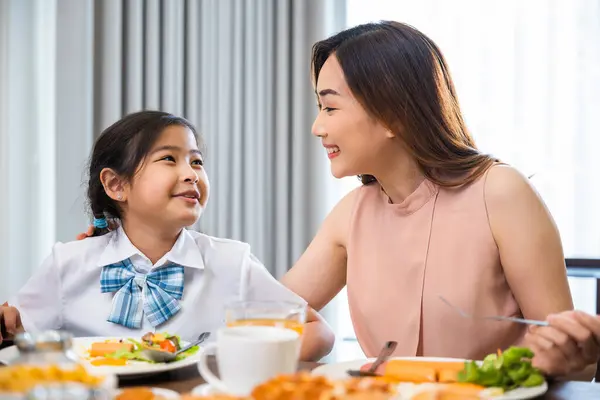 Asian family breakfast. smiling mother and child daughter having breakfast on food table, Healthy food at home before go to school, Mom and little preschooler have fun eating meal together