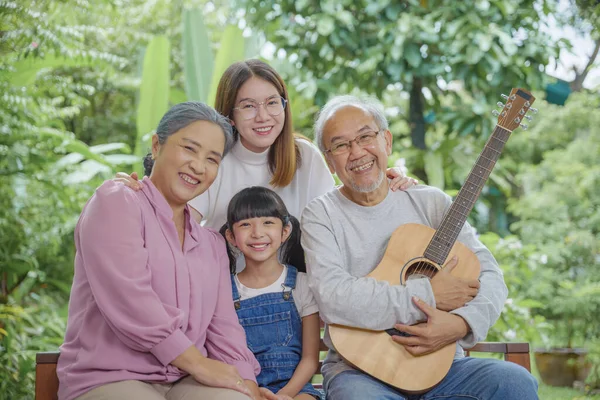Happy family Asian senior elderly man or grandfather playing guitar while his grandmother and granddaughter singing song together outdoors at home, Activity family, Enjoying lifestyle senior older