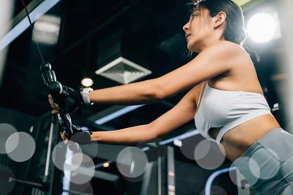 Beautiful woman working out indoors, using a pull-down weight machine to train her arms and build muscle. fitness center health workout concept