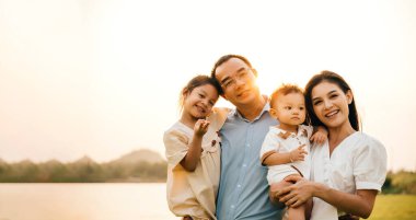 Mutlu bir grup çocuk ve ebeveyn parkta gülüyor ve eğleniyorlar, dört kişilik neşeli bir aile güneşin sıcaklığının ve açık havanın güzelliğinin tadını çıkarıyorlar, Aile Günü.