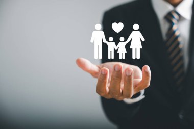 Aile merkezi bakım, iş adamı koruyucu jesti genç aile siluetini tamamlıyor. Sağlık ve ev sigortası ikonu korumayı, aile destek konseptini sembolize eder. Aile hayat sigortası