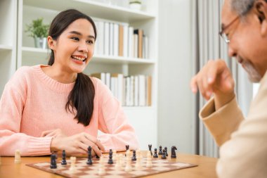 Beautiful young smile woman having fun sitting playing chess game with senior elderly at home, nurse caregiver in nursing home for leisure, Happy active retired people, Healthcare and medical concept