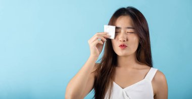 Facial Beauty Treatment Hygiene skin. Asian beautiful young woman removing cosmetic make up using pad cotton face cleaner disc, studio shot isolated on blue background, Happy female cleaning eyes