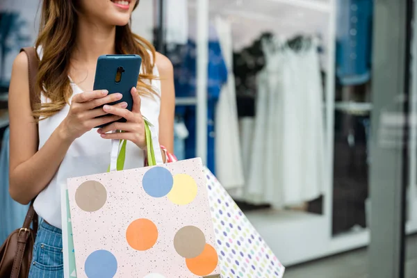 A fashionable woman multitasking with shopping bags and a cellphone enjoys the convenience of online shopping. Shes browsing the latest fashion and accessories while on the go.