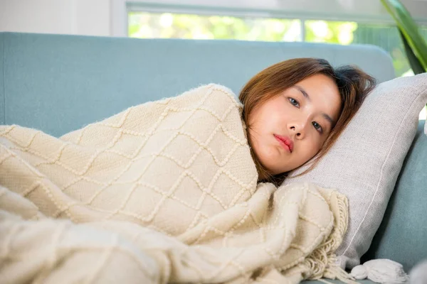 Asian sick woman cold high fever covered with blanket resting sleeping at home, young woman have problem with headache lying on sofa in living room, Unhappy sick girl, person tired