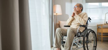 Asian senior man disabled sitting alone in wheelchair looking through window at hospital, lonely elder thoughtful sad old man look outside windows in bedroom at retirement home, feel depressed lonely