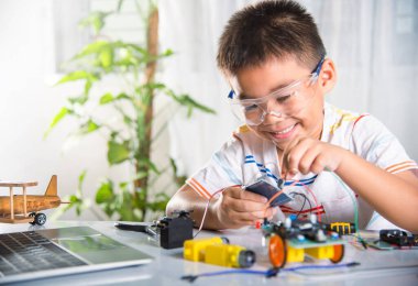 Asyalı çocuk, Arduino robot arabasıyla sensör çipine enerji ve sinyal kablosu takıyor, küçük çocuk oyuncaklarla uzaktan öğreniyor, STEAM eğitim teknolojisi dersleri.