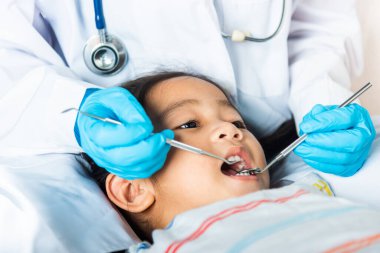 Diş hekimi çocuk sağlık muayenesi. Doktor küçük bir çocuğun ağız boşluğunu inceliyor diş boşluğunu kontrol etmek için ağız aynası kullanıyor, Asyalı dişçi gülümseyen küçük kız için muayene prosedürü yapıyor.