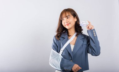 Kırık koluna rağmen, bir atel takan kadın gülümsüyor. Acil sağlık giderlerini kredi kartıyla karşılıyor. Beyaz arka planda askılık desteği olan mutlu bir Asyalı kadın. Yara çok açık..