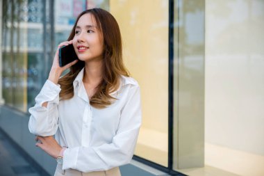 Gülümseyen esmer patron müşteriyle konuşuyor. Şehir caddesinde cep telefonu kullanan beyaz gömlekli bir iş kadını. İş için telefon görüşmesi modern iletişim teknolojisidir..