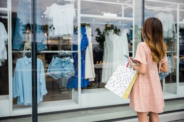 Alışveriş torbaları taşıyan bir kadın satış ilanı veren bir butik giyim mağazasının önünden geçiyor. Moda kıyafetlerdeki indirimler müşterilerin hoşuna gider.
