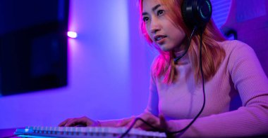 Happy Gamer endeavor plays online video games tournament with computer neon lights, young woman wearing gaming headphones intend to do playing live stream games online at home