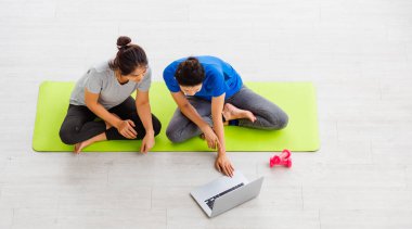 İki Asya yaşam tarzı yetişkin ve genç kadın spor kıyafetleri içinde yerde, dambıllarla oturuyorlar yoga stüdyosundaki eğitim videoları için dizüstü bilgisayara bakıyorlar spor için sağlıklı egzersiz yapıyorlar.