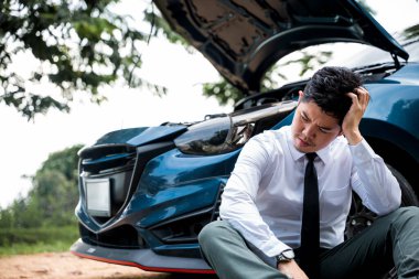 Kırsal yolda kapüşonlu bozuk arabasının yanında oturan bir adam yol kenarında yardım istiyor. Araba sorunu ve hayal kırıklığı kavramı.