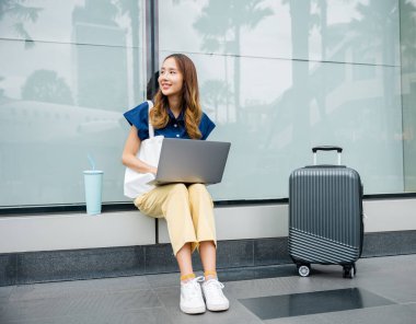 Bir iş kadını, uçuşunu beklerken birden fazla iş yapar, bilgisayarını havaalanındaki bir çıkıntının üzerinde verimli olmak için kullanır..
