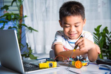 Asian kid boy assembling the Arduino robot car homework project at home, Little child tighten the nut with a screwdriver to assemble car toy, creating electronic AI technology workshop school lesson
