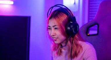 Happy Gamer endeavor plays online video games tournament with computer neon lights, young woman wearing gaming headphones intend to do playing live stream games online at home