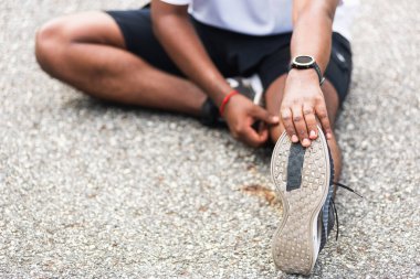 Kapatın Asyalı genç sporcu spor koşucusu siyah adam kol saati takıyor ayak parmaklarını uzatıyor bacaklarını ve dizlerini esnetiyor açık hava parkına koşmadan önce spor konseptinden önce sağlıklı egzersiz.
